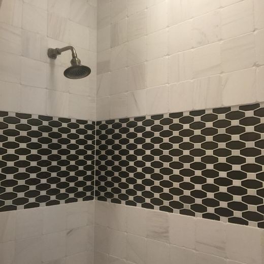 Primary bathroom shower with marble tile and dark hexagon mosaic band — Storybook Homes NJ