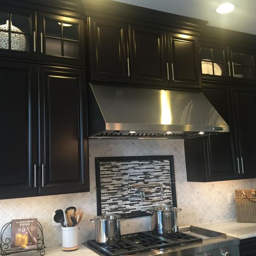 Kitchen with espresso cabinetry, stainless range hood, and mosaic backsplash — Storybook Homes NJ